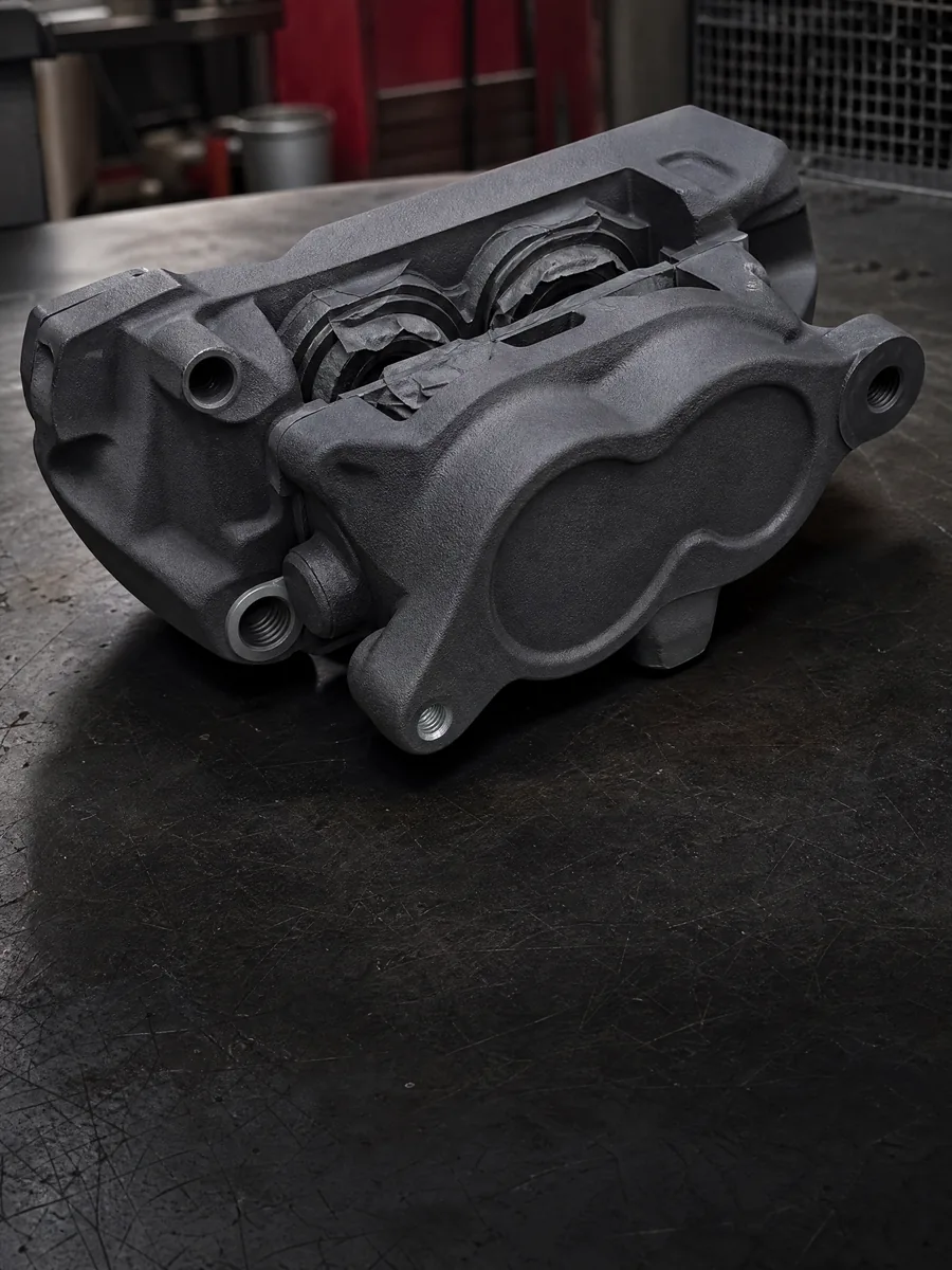 Matte graphite Cerakoted motorcycle brake caliper on a dark shop workbench