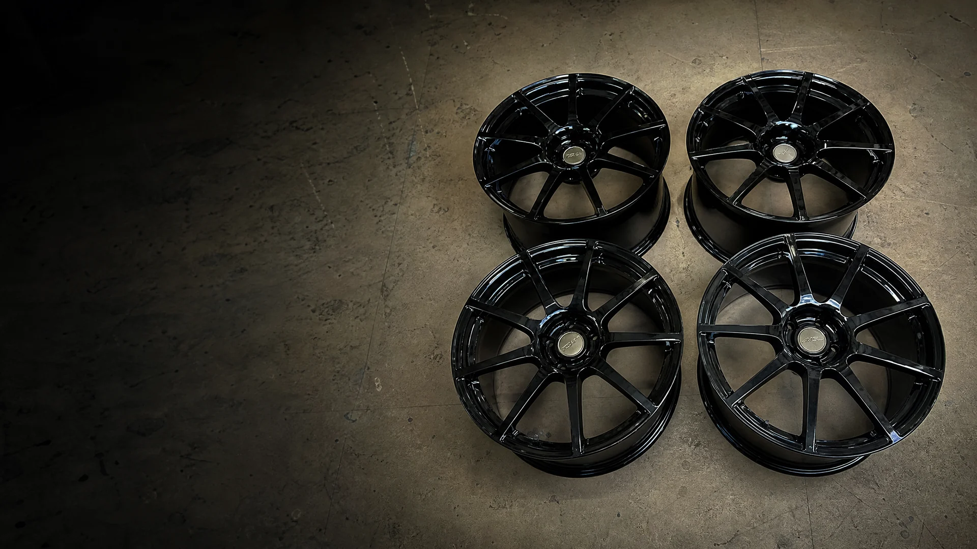 Four gloss-black powder-coated wheels on a shop floor